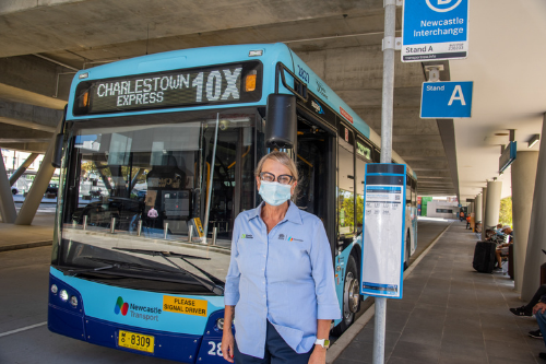 Female driver wearing a face mask standing in front of bus route 10X