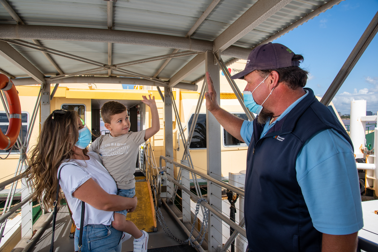 Woman holding a young boy who is high fiving a male ferry staff member